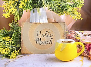 A bouquet of mimosa flowers, a piece of paper with the inscription hello March and a yellow cup of coffeeGenerated image