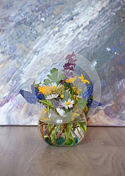 Bouquet of mixed spring flowers in a little glass, round vase. Corydalis cava, Muscari armeniacum, camomile, dandelion in a vase