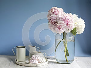 A bouquet of multi-colored hydrangeas in a five-liter jar on a blue wall background