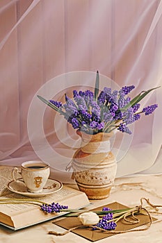 Bouquet of muscari flowers in a vintage vase. Cup of coffee, book and romantic flowers.