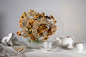 Bouquet of orange helenium with wild grape leaves in a fluted glass vase against a dark blue wall