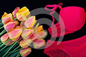 A bouquet of orange-red tulips and bright red women underwearbra and pantie on black background.Romantic lingerie.Flat lay.Ð¡
