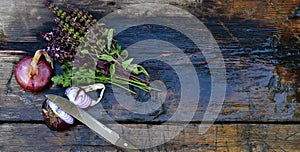 A bouquet of parsley greens with basil sprigs with flowers on a wooden wet surface. Next to the purple bow and knife