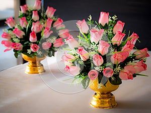 Bouquet of pink artificial flowers on gold color tray with pedestal.