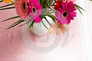 Bouquet of pink daisies in white vase on pink background, colorful flowers view above