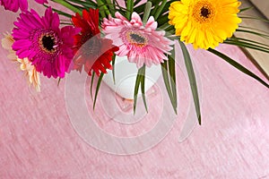 Bouquet of pink daisies in white vase on pink background, colorful flowers view above