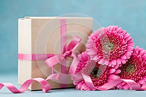 Bouquet of pink gerbera flowers and gift box with ribbon on turquoise table. Greeting card for Birthday, Woman or Mothers Day.