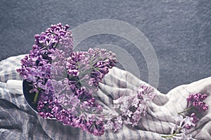 Bouquet of pink lilacs in a cup on a striped cotton drape scarf on a dark surface, toned, top view