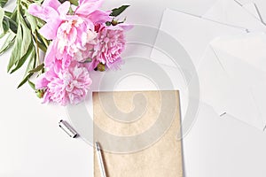 A bouquet of pink peonies on office desk. notebook, envelope, pen and a coffee mug. feminine workplace, top view, copy space