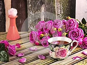 A bouquet of pink peony roses, a cup of tea decorated with roses, a candle in the form of a rose.