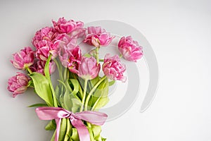 Bouquet of pink peony tulips tied with a pink bow. Spring flowers on the white background and place for text. Festive concept for