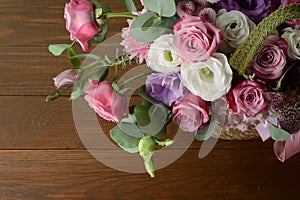 Bouquet of pink roses in basket on wooden background closeup. Roses and eustoma flowers greeting card, floristics