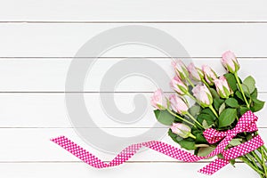 Bouquet of pink roses decorated with ribbon on white wooden background. Top view