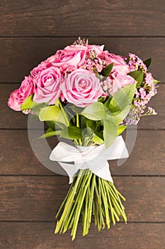 Bouquet of pink roses decorated with white bow of ribbon on wooden background