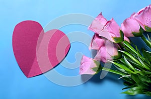 Bouquet of pink roses and red paper heart on blue background