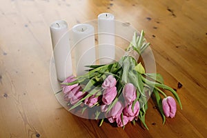 Bouquet of pink tulips on a beautiful wooden background with candles rewinded with craft thread