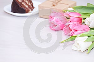 Bouquet of pink tulips, chocolate cake. pressent box on white wooden background. Copy space, close up. Mother`s, women`s day
