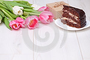 Bouquet of pink tulips, chocolate cake. pressent box on white wooden background. Copy space, close up. Mother`s, women`s day