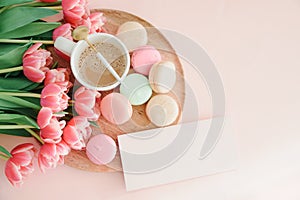 Bouquet of pink tulips, cup of coffee and macaroons on pink background. Anniversary celebration concept. Copy space. Top view