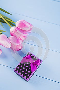 Bouquet of pink tulips with gift box on blue wooden background