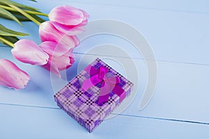 Bouquet of pink tulips with gift box on blue wooden background