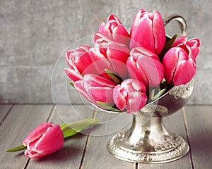 Bouquet of pink tulips in metal vase on wooden background