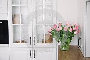 Bouquet of pink tulips in a transparent vase, on kitchen. Flowers in interior.