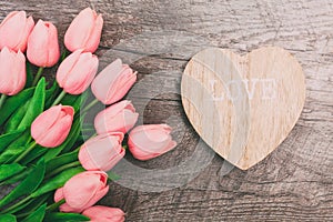 Bouquet of pink tulips and a valentine in the shape of a heart from wood, on a wooden background