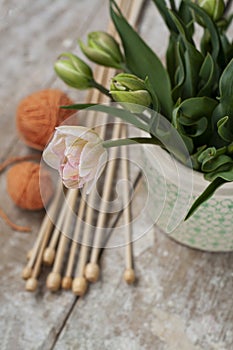 Bouquet of pink tulips in vase, near the vase are wooden spokes and a few tangles of orange threads