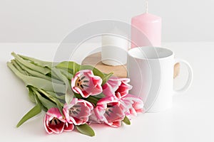 Bouquet of pink tulips, white mug and candles on a white table