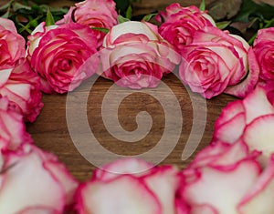 A bouquet of pink and white roses arranged in a heart shape on a wooden surface