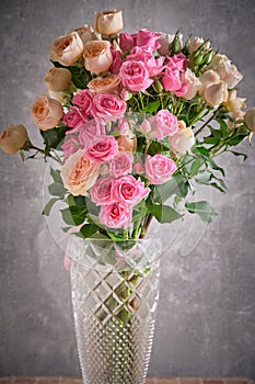 Bouquet of pink and white roses in vase on grey background.