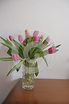 bouquet of pink and yellow tulips in vase closeup across white all on the wooden drawer. Interior detail. Hotel interior