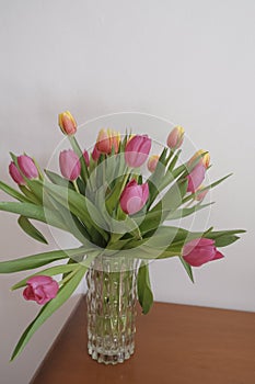 bouquet of pink and yellow tulips in vase closeup across white all on the wooden drawer. Interior detail. Hotel interior