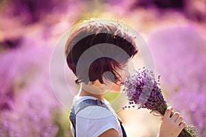 Bouquet portrait of happy cute little girl with bob haircut sniffing lavender bouquet in lavender field with purple flowers around