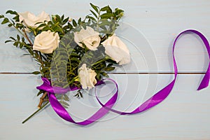 Bouquet of pretty flowers with and bright purple gift ribbon bow on turquoise shabby chic background, top view
