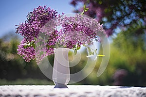 Bouquet of purple lilacs in a white vase on the table