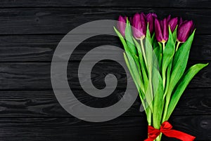 Bouquet of purple spring tulip flowers on a black wooden background. Flat lay. Copy space. Mothers Day