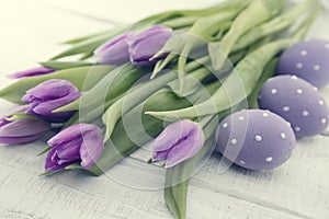 Bouquet of purpleviolet tulips and painted easter eggs on white rustic wooden background with copy space for message. Holiday