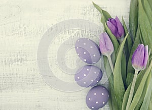 Bouquet of purpleviolet tulips and painted easter eggs on white rustic wooden background with copy space for message. Holiday