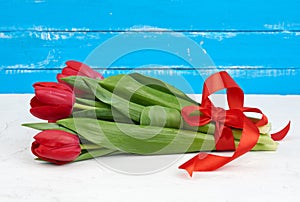 Bouquet of red blooming tulips with green stems and leaves tied with a red silk ribbon