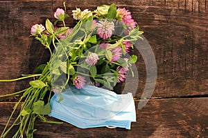Bouquet of red clover flowers and blue pandemic face mask on wooden background outdoors. Spring or summer still life