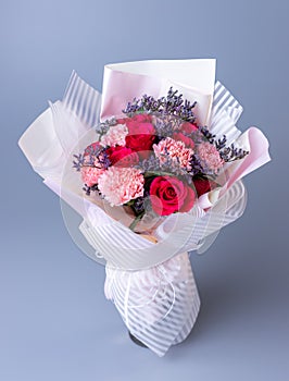 Bouquet of red and pink flowers wrapped in festive paper on a blue background.