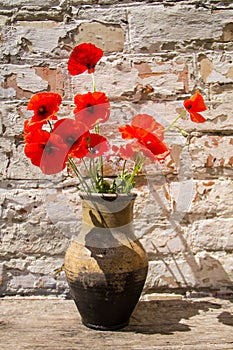 Bouquet of red poppies in clay jug on wooden table against old brick wall