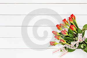 Bouquet of red roses decorated with lace on white wooden background