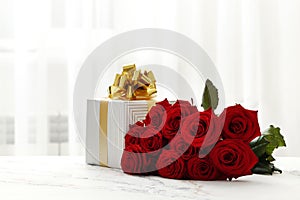 A bouquet of red roses and a gift box on the table in the interior. Love confession.