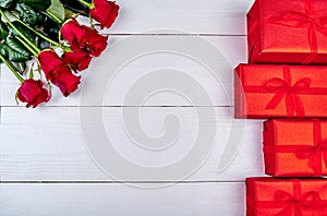 Bouquet of red roses and gift boxes on white wooden background, copy space. Greeting card mockup for Saint Valentines Day.