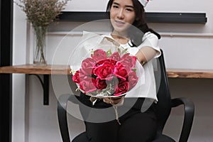 Bouquet of red roses is held on hands of attractive young Asian woman in office on valentine`s day. Love and romance concept.