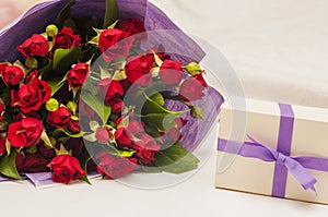 Bouquet of red roses in purple wrapping paper and gift box with purple ribbon on white background.