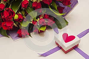 Bouquet of red roses in purple wrapping paper and gift box with red heart and purple ribbon on white background.